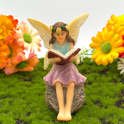 A seated miniature fairy reading an open book.
