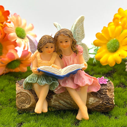 Story time fairies. Two fairies miniatures seated on a log with one fairy reading a story book.