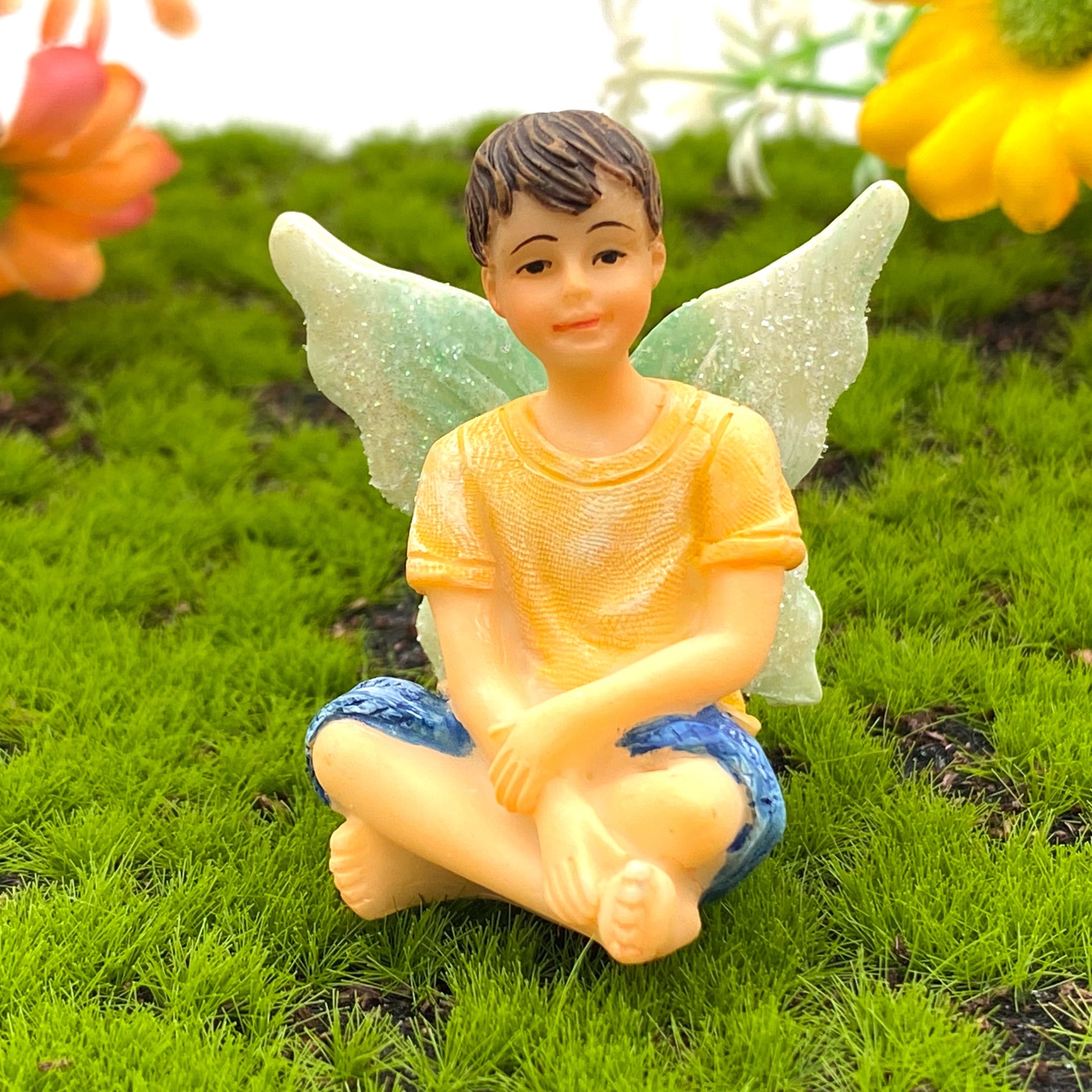 A boy fairy miniature figurine seated with crossed legs.